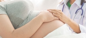 אשה בהיריון שוכבת על מיטת בית חולים ולידה רופאה אוחזת בידה